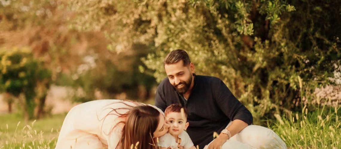 A joyful family with parents and a baby enjoying a sunny day outdoors on a picnic.