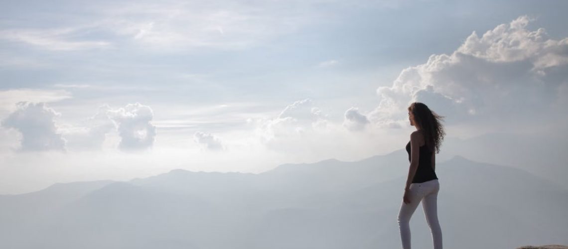 A woman standing on a mountain cliff, enjoying the sunrise and panoramic views.